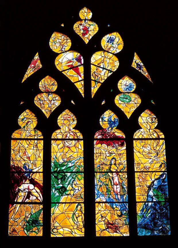 A tall stained glass window with panels in vibrant yellows, oranges, blues, and greens. The pane features abstract, flowing peinture-inspired designs and figures—people, animals, and plants—outlined in black and glowing with amour against a dark background.