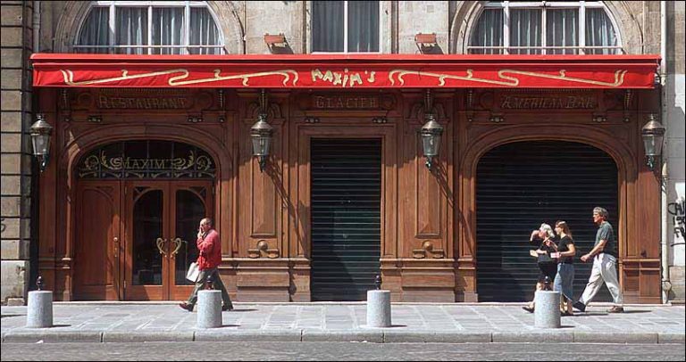 A street view of TWIN MAXIM'S restaurant with ornate wooden doors and closed black shutters. A red awning with yellow accents and MAXIMS written on it covers the entrance, as four people walk past—one man to the left, three to the right.