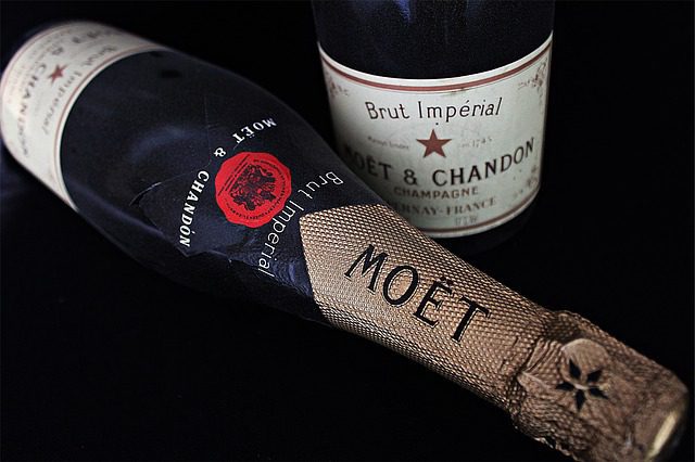 A close-up of two Moët & Chandon Champagne bottles on a black surface; one bottle lies down, revealing its foil-wrapped neck and label, while the other stands upright, showcasing the Brut Impérial label—the heart and soul of celebration.