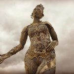 A tall, ornate metallic sculpture of a woman stands against a cloudy sky at BurningMan. Intricately detailed with swirling patterns, gears, and filigree, it blends fantasy and steampunk—a striking figure often seen in unforgettable BurningMan photos.