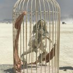 A life-sized, ghostly humanoid sculpture with long hair appears to run inside a large, pale birdcage at Burning Man. Torn brown fabric hangs from the bars. The cage rests on a barren, dusty plain under a hazy sky, with distant figures and mountains behind.