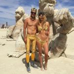 A man and woman in gold costumes pose in front of large, sculpted gorilla figures on a desert playa under a blue sky—one of those BurningMan photos that capture the surreal, almost photos impossibles moments found at this iconic festival.