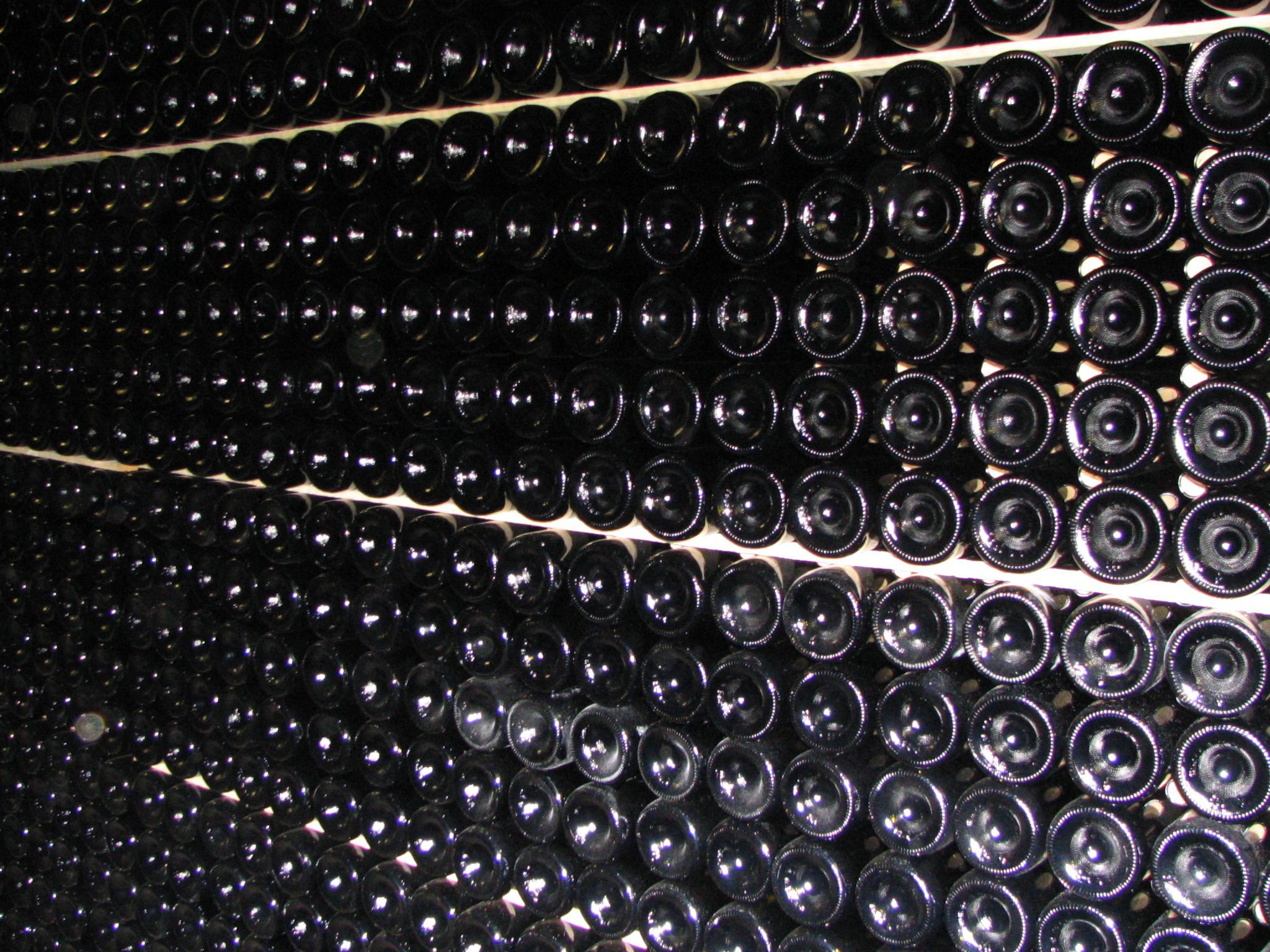 Dans une cave, des rangées de bouteilles de vin en verre foncé sont empilées horizontalement, le fond tourné vers l'extérieur. Des lignes nettes et parallèles sur les étagères créent un motif géométrique - une inspiration idéale pour ceux qui cherchent à acheter du vin en ligne et à agrandir leur collection. 