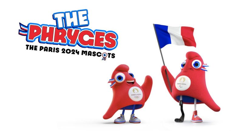 Two red, soft, triangular mascots called “The Phryges” stand together. One mascot holds a French flag and has a prosthetic leg. Both wear sneakers and Paris 2024 Olympic badges. “THE PHRYGES PARIS 2024 OLYMPIC MASCOTS” appears above them in bold text.